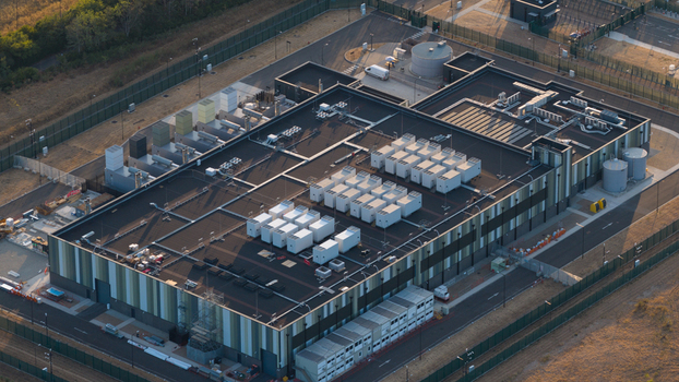 Aerial view of a modern industrial data center facility with rooftop HVAC units secure perimeter fencing and surrounding grounds in Bracknell England United Kingdom.