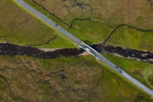 Aerial view of a road crossing a bridge over a dark stream in the rural landscape near Ballachulish Scotland United Kingdom.
