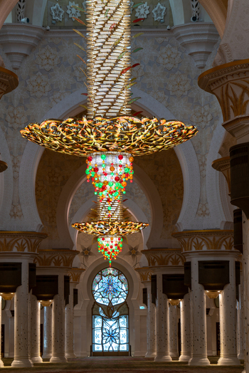 View of a massive ornate chandelier with colorful crystals hanging from a vaulted ceiling in a grand mosque hall with marble columns and floral patterns in Dubai Dubai United Arab Emirates. View of a massive ornate chandelier with colorful crystals hanging from a vaulted ceiling in a grand mosque hall with marble columns and floral patterns in Dubai Dubai United Arab Emirates.