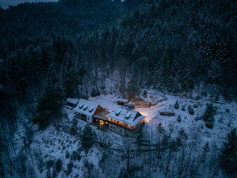 Aerial view of a cozy illuminated cabin nestled in a dense snow covered evergreen forest at dusk in Spania Dolina Banska Bystrica Region Slovakia. Aerial view of a cozy illuminated cabin nestled in a dense snow covered evergreen forest at dusk in Spania Dolina Banska Bystrica Region Slovakia.