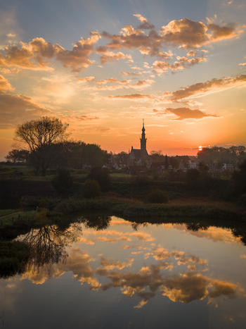 Aerial view of the historic town of Veere with its prominent church spire silhouetted against a golden sunset reflected in the calm water Veere Zeeland Netherlands.
