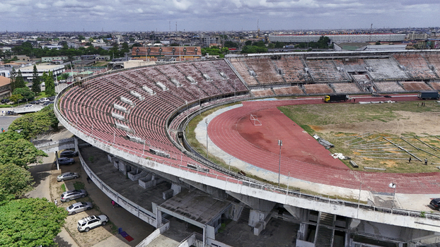 Aerial view of National Stadium Surulere Lagos with its curved red seating tiers athletic track and the surrounding urban skyline under a cloudy sky Lagos Lagos Nigeria. Aerial view of National Stadium Surulere Lagos with its curved red seating tiers athletic track and the surrounding urban skyline under a cloudy sky Lagos Lagos Nigeria.