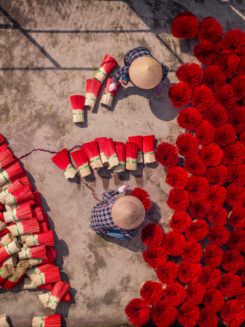 Aerial view of workers wearing traditional conical hats arranging bundles of vibrant red incense sticks during the drying process in Vietnam. Aerial view of workers wearing traditional conical hats arranging bundles of vibrant red incense sticks during the drying process in Vietnam.