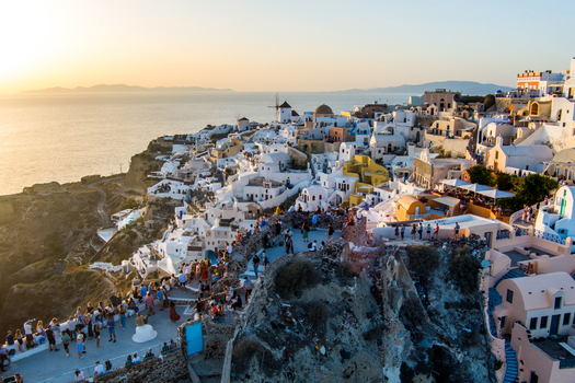 Oia Santorini Greece 21 September 2026 Aerial view of the iconic white buildings and blue domed churches of Oia at sunset with crowds of people gathered. Oia Santorini Greece 21 September 2026 Aerial view of the iconic white buildings and blue domed churches of Oia at sunset with crowds of people gathered.