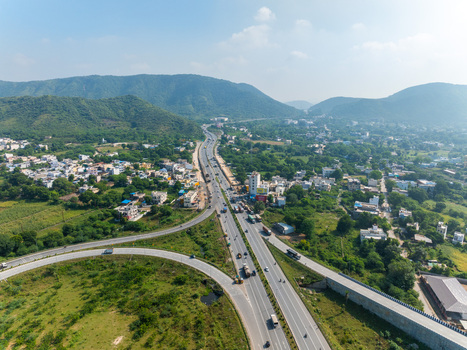 Aerial view of a highway junction surrounded by lush green hills scattered residential buildings and open fields in Udaipur Rajasthan India. Aerial view of a highway junction surrounded by lush green hills scattered residential buildings and open fields in Udaipur Rajasthan India.