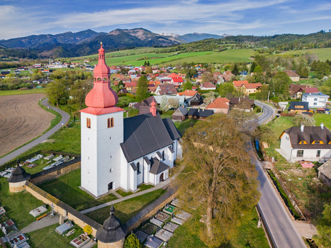 Aerial view of the Church of Saint Ladislaus with its red onion dome and stone wall cemetery surrounded by green fields and distant mountains in Liptovske Matiasovce Zilina Region Slovakia.