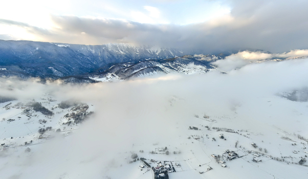 Brasov Romania 21 September 2026 Aerial view of the snow covered Carpathian Mountains and the valley of Brasov partially obscured by low hanging clouds under a bright winter sky. Brasov Romania 21 September 2026 Aerial view of the snow covered Carpathian Mountains and the valley of Brasov partially obscured by low hanging clouds under a bright winter sky.