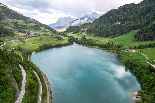 Aerial view of the turquoise Lac du Vernex surrounded by lush green hills and alpine mountains in Rossiniere Vaud Switzerland.