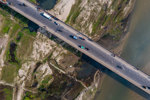 Aerial view of a bridge spanning a river with vehicles and people moving across surrounded by rural landscape in Panchagarh Rangpur Division Bangladesh. Aerial view of a bridge spanning a river with vehicles and people moving across surrounded by rural landscape in Panchagarh Rangpur Division Bangladesh.