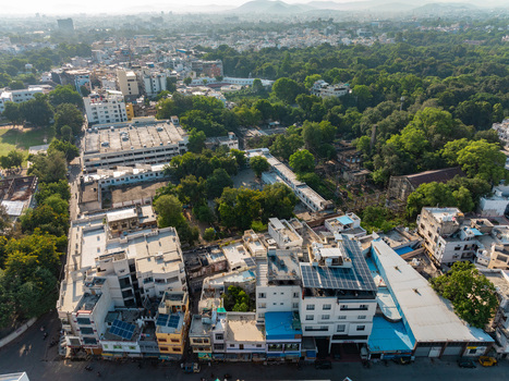 Aerial view of the urban landscape of Udaipur featuring dense residential buildings solar panels on rooftops lush green trees and distant hills in Udaipur Rajasthan India.