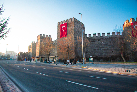 View of Kayseri Castle with stone walls and Turkish flags under a clear blue sky next to a city street with people in Kayseri Kayseri Turkiye. View of Kayseri Castle with stone walls and Turkish flags under a clear blue sky next to a city street with people in Kayseri Kayseri Turkiye.