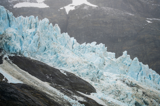 View of the Drygalski Fjord glacier with jagged blue ice formations snow covered mountain slopes and dark rocky terrain in South Georgia and the South Sandwich Islands.