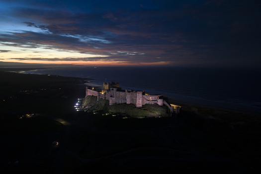 Aerial view of Bamburgh Castle illuminated on a rocky cliff overlooking the North Sea at twilight Bamburgh England United Kingdom. Aerial view of Bamburgh Castle illuminated on a rocky cliff overlooking the North Sea at twilight Bamburgh England United Kingdom.