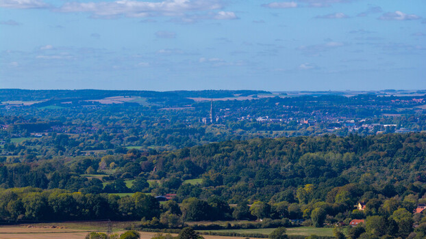 Aerial view of the rolling landscape of Pepperbox Hill with Salisbury Cathedral in the distance surrounded by lush green trees and fields in Salisbury England United Kingdom. Aerial view of the rolling landscape of Pepperbox Hill with Salisbury Cathedral in the distance surrounded by lush green trees and fields in Salisbury England United Kingdom.