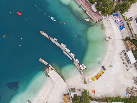 Aerial view of the turquoise waters and sandy beach of Ksamil with wooden piers moored boats and colorful pedal boats along the coastline in Ksamil Vlore County Albania. Aerial view of the turquoise waters and sandy beach of Ksamil with wooden piers moored boats and colorful pedal boats along the coastline in Ksamil Vlore County Albania.