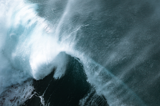 Aerial view of a large ocean wave breaking with white foam and spray in the deep blue sea at Narrabeen New South Wales Australia.