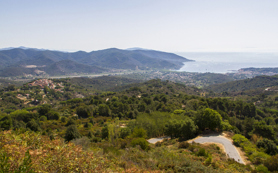 View of winding roads through lush green hillsides leading to a coastal town nestled by the sea a serene vista under a clear sky Elba Tuscany Italy. View of winding roads through lush green hillsides leading to a coastal town nestled by the sea a serene vista under a clear sky Elba Tuscany Italy.