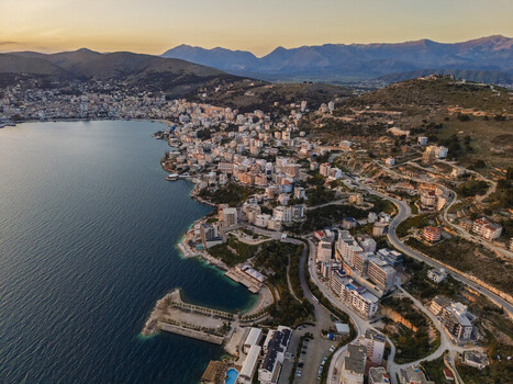 Aerial view of the coastal city featuring dense urban architecture a scenic bay and a mountainous backdrop during the golden hour Saranda Vlore County Albania. Aerial view of the coastal city featuring dense urban architecture a scenic bay and a mountainous backdrop during the golden hour Saranda Vlore County Albania.