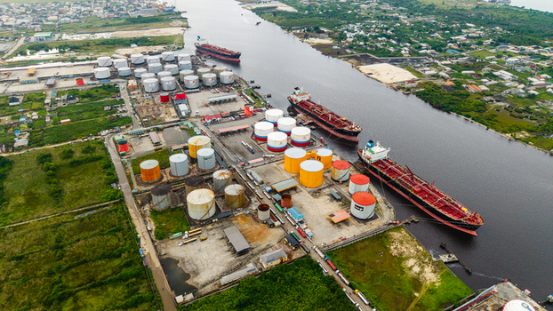 Aerial view of the oil terminal in Satellite Town featuring large storage tanks industrial infrastructure and cargo ships docked along the river in Lagos Lagos Nigeria.