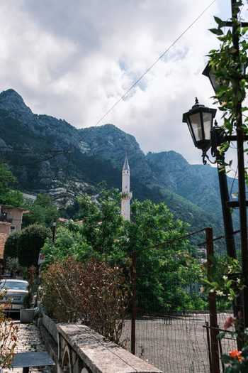 View of the white minaret of a mosque rising above lush green trees with the rugged Skanderbeg Mountains in the background under a cloudy sky in Kruje Durres County Albania.