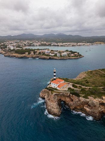 Aerial view of the Portocolom Lighthouse on a rocky cliff overlooking the blue sea and coastal town Portocolom Balearic Islands Spain. Aerial view of the Portocolom Lighthouse on a rocky cliff overlooking the blue sea and coastal town Portocolom Balearic Islands Spain.