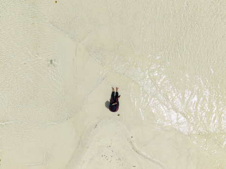 Aerial view of a person sitting on the shore surrounded by the light soft sand meeting the clear water at Cemara Kecil Island Karimunjawa Central Java Indonesia.