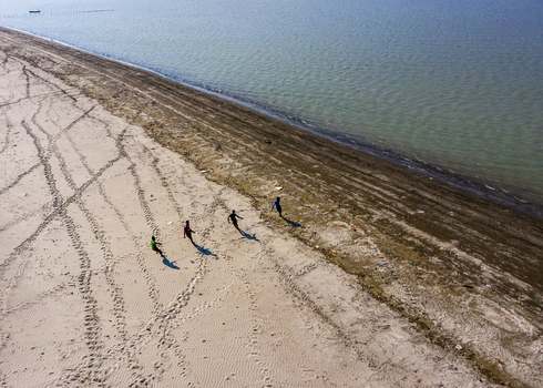 Aerial view of people walking along the sandy beach of Kuakata with footprints visible on the shore and calm water in Kuakata Barisal Division Bangladesh. Aerial view of people walking along the sandy beach of Kuakata with footprints visible on the shore and calm water in Kuakata Barisal Division Bangladesh.
