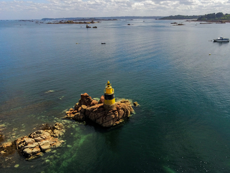 Aerial view of the yellow and black beacon on a rocky islet surrounded by clear blue sea in Ile de Brehat Brittany France.