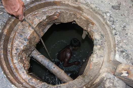Dhaka Bangladesh 18 April 2018 View of a sewer worker inside a manhole cleaning the drainage system with dark water and concrete surroundings. Dhaka Bangladesh 18 April 2018 View of a sewer worker inside a manhole cleaning the drainage system with dark water and concrete surroundings.