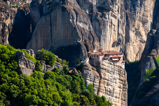 Aerial view of the historic monastery at Meteora perched on a dramatic rock formation surrounded by lush green forest and steep cliffs in Trikala Greece. Aerial view of the historic monastery at Meteora perched on a dramatic rock formation surrounded by lush green forest and steep cliffs in Trikala Greece.