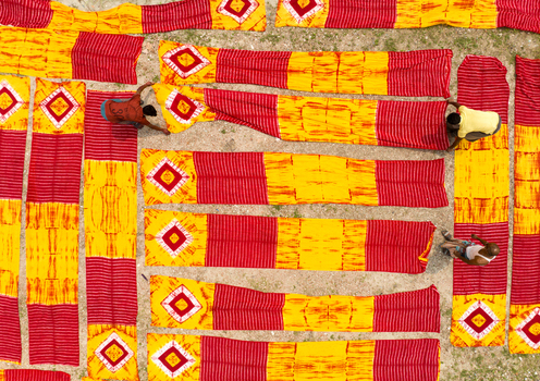 Narayanganj Bangladesh 30 March 2026 Aerial view of vibrant red and yellow fabrics laid out to dry creating a striking geometric pattern against the earthy ground.