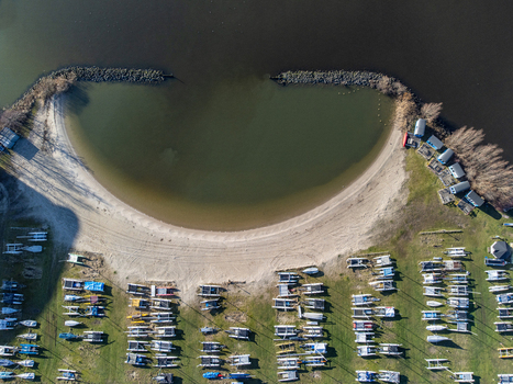 Aerial view of boats lined up neatly on the green grass facing the sandy beach and the calm water of Marinaweg Almere Flevoland Netherlands. Aerial view of boats lined up neatly on the green grass facing the sandy beach and the calm water of Marinaweg Almere Flevoland Netherlands.
