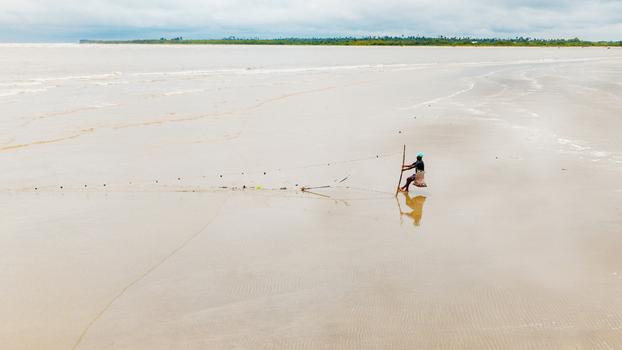 Aerial view of a lone fisherman standing in the shallow waters of Ibeno Beach with his fishing net set against the vast coastline of Kwa Ibo Akwa Ibom Nigeria.