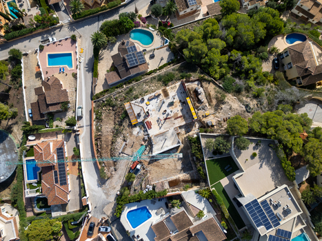 Aerial view of a construction site with a crane surrounded by residential houses with swimming pools and solar panels in Moraira Valencian Community Spain.