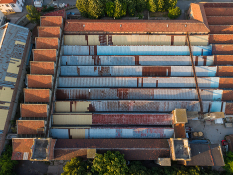Aerial view of an industrial factory building with rows of weathered corrugated metal roofs and red tiles surrounded by trees in Varna Varna Bulgaria. Aerial view of an industrial factory building with rows of weathered corrugated metal roofs and red tiles surrounded by trees in Varna Varna Bulgaria.