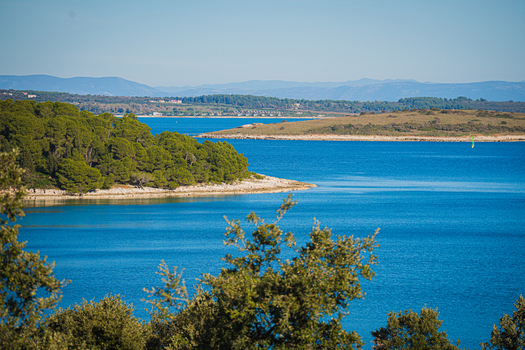 View of the tranquil turquoise sea meeting the rugged coastline verdant trees and distant mountains under a clear sky Pula Istria County Croatia.