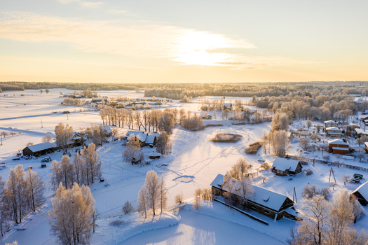 Aerial view of a serene winter landscape in Latvia featuring a frozen lake surrounded by snow covered trees and rustic houses bathed in the warm glow of the golden hour Latvija. Aerial view of a serene winter landscape in Latvia featuring a frozen lake surrounded by snow covered trees and rustic houses bathed in the warm glow of the golden hour Latvija.