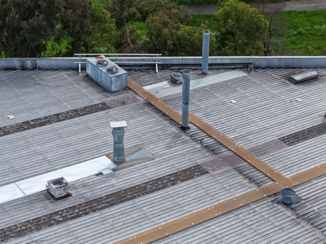 Aerial view of an industrial factory roof featuring metal corrugated surfaces ventilation pipes and maintenance walkways in Melbourne VIC Australia.
