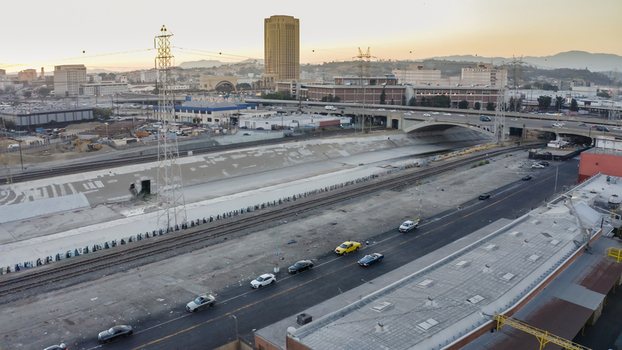 Aerial view of the Los Angeles River channel with adjacent railway tracks a highway overpass and urban buildings under a soft sunset sky in Los Angeles California United States. Aerial view of the Los Angeles River channel with adjacent railway tracks a highway overpass and urban buildings under a soft sunset sky in Los Angeles California United States.