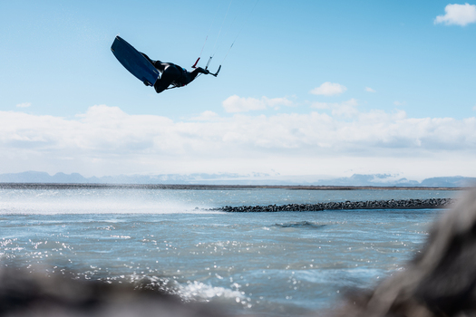 View of a kitesurfer performing a high jump over the water with mountains in the background in Skaftarhreppur Iceland.