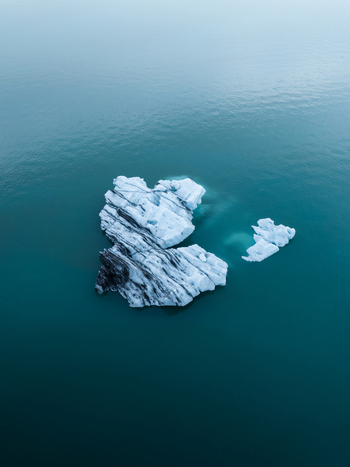 Aerial view of a solitary iceberg drifts in the lagoon s expanse its icy blue contrasting with the deep turquoise waters Jokulsarlon Sveitarfélagið Hornafjörður Iceland. Aerial view of a solitary iceberg drifts in the lagoon s expanse its icy blue contrasting with the deep turquoise waters Jokulsarlon Sveitarfélagið Hornafjörður Iceland.