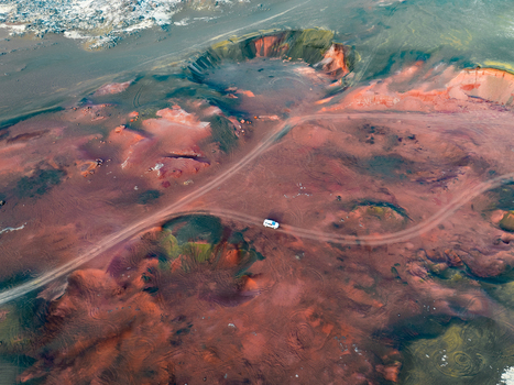 Aerial view of a white off road vehicle driving on a dirt track through the colorful volcanic landscape of Reykjanesbaer Iceland. Aerial view of a white off road vehicle driving on a dirt track through the colorful volcanic landscape of Reykjanesbaer Iceland.