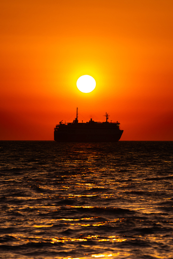 View of a ferry silhouetted against a vibrant orange sunset over the sea Greece. View of a ferry silhouetted against a vibrant orange sunset over the sea Greece.