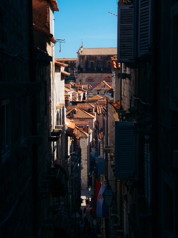 View of a narrow stone street with red tiled rooftops a Croatian flag and people walking in the historic Dubrovnik Old Town Dubrovnik Dubrovnik Neretva County Croatia. View of a narrow stone street with red tiled rooftops a Croatian flag and people walking in the historic Dubrovnik Old Town Dubrovnik Dubrovnik Neretva County Croatia.