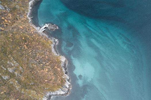 Aerial view of the rugged coastline of Senja with turquoise waters rocky cliffs and a small wooden pier extending into the sea in Senja Troms Norway.