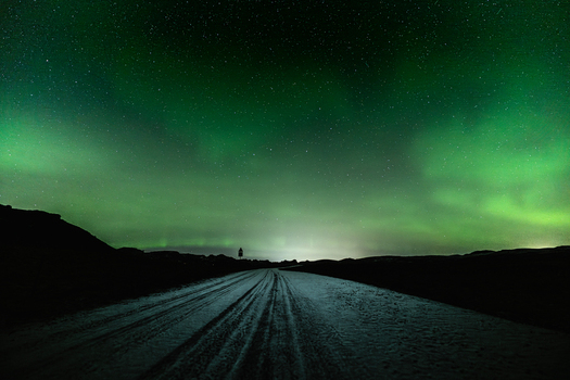 View of an endless road reflecting the ethereal green glow of the aurora borealis under a starlit sky Krysuvikurkirkja Hafnarfjardarkaupstadur Iceland.