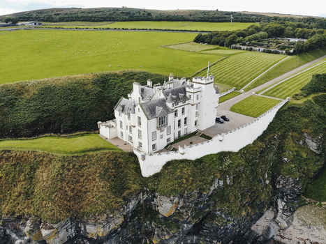 Aerial view of Dunbeath Castle perched on a dramatic cliff edge overlooking the coast surrounded by lush green fields and manicured lawns in Dunbeath Scotland United Kingdom. Aerial view of Dunbeath Castle perched on a dramatic cliff edge overlooking the coast surrounded by lush green fields and manicured lawns in Dunbeath Scotland United Kingdom.