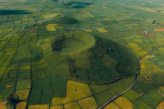 Aerial view of Pico Dona Joana volcanic crater surrounded by a patchwork of green agricultural fields and stone walls in Feteira Acores Portugal.