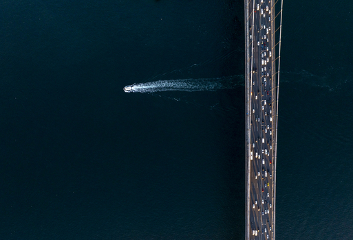 Aerial view of Fatih Sultan Mehmet Bridge spanning the Bosphorus with heavy traffic on the deck and a small boat leaving a wake in the dark water below in Beykoz Istanbul Turkiye. Aerial view of Fatih Sultan Mehmet Bridge spanning the Bosphorus with heavy traffic on the deck and a small boat leaving a wake in the dark water below in Beykoz Istanbul Turkiye.