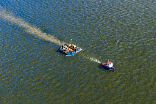 Aerial view of a small tugboat towing a flat barge on the Nordre alv river in Vastra Gotaland County Sweden.